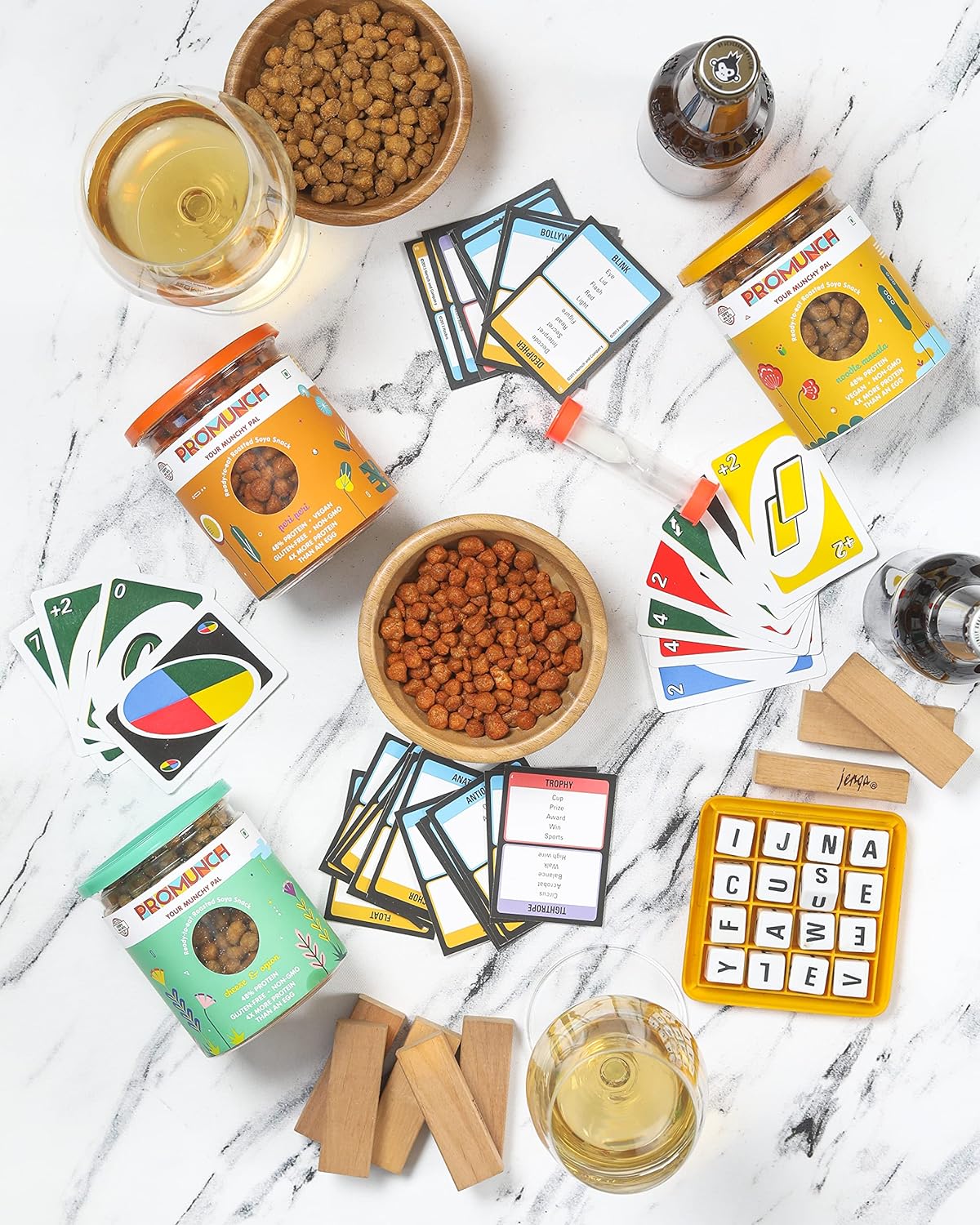 A cozy game night setup with cards, board games, drinks, PROMUNCH soya snacks, and lit candles, creating the perfect vibe for fun and laughter with friends.